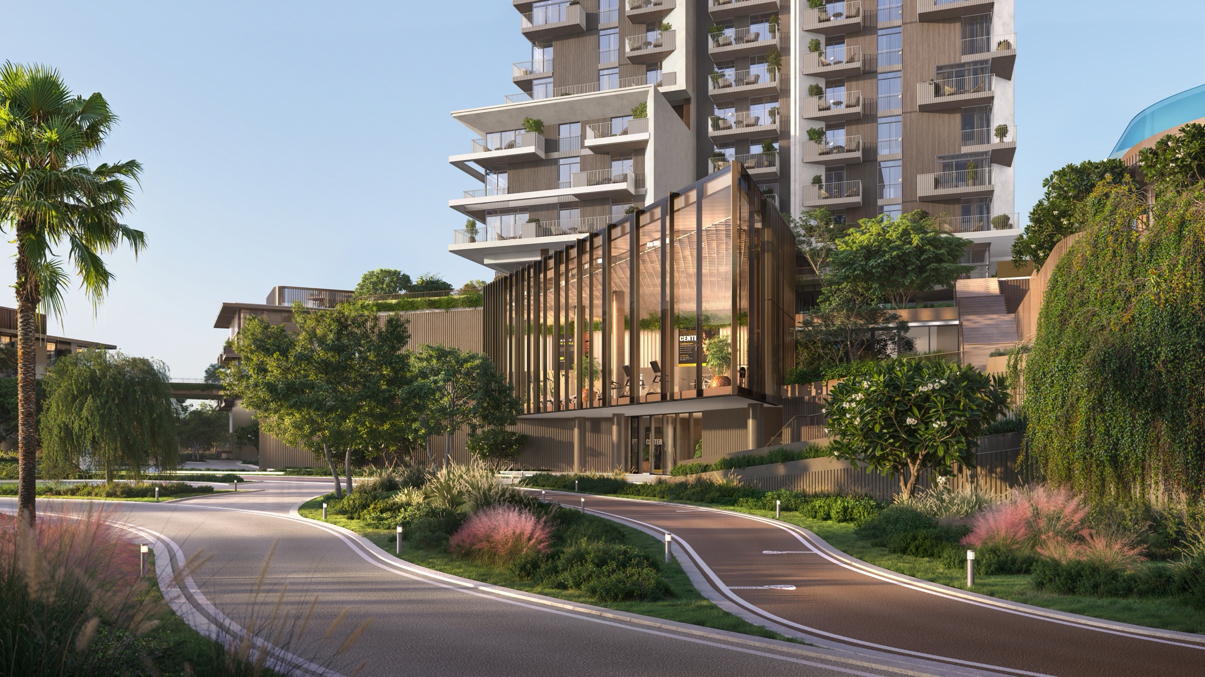 Glazed pavilion with a sawtooth roof at the foot of a balcony tower, seen across a curving road and pink grasses, a building render for Grid at Rise by Athlon in Wadi Al Safa 5, Dubailand.